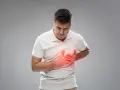 Mężczyzna w białej koszulce trzyma się za klatkę piersiową, odczuwając niepokój. Czerwony blask podkreśla ból.