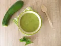 Zucchini Brei Baby: Eine Schüssel grüner Zucchinipüree, daneben eine Zucchini und ein Holzlöffel.