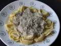 Tortellini de queso cubiertos con una cremosa salsa de champiñones y pimienta negra, servidos en un plato blanco con espirales decorativas.
