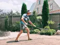 Un homme en chapeau et short utilise un râteau pour faire une place de parking dans son jardin. Le soleil brille sur la pelouse.