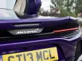 Fioletowy McLaren GT z otwartymi drzwiami, widok na tył z logo i tablicą rejestracyjną.