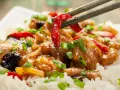 Schab po chińsku z ryżem, papryką i szczypiorkiem. Pałeczki podnoszą kawałek papryki z dania.
