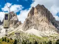 Cabine della funivia salgono verso le imponenti vette del Sassolungo, un anello di roccia maestoso sotto un cielo azzurro con nuvole bianche.