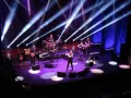 Zespół muzyczny na scenie, oświetlony niebieskimi i fioletowymi światłami. Wokalista na pierwszym planie, gitarzyści, basista, skrzypek i perkusista. Jak liczyć takty w muzyce, można się nauczyć, obserwując ich rytm.