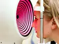 Esame oculistico: una donna guarda un dispositivo che proietta una mappa corneale a spirale rosa e nera.