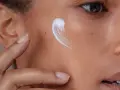 Creme wird auf die Wange einer Person mit fettiger, unreiner Haut aufgetragen.