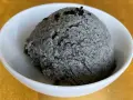 Ein Löffel cremiges Sesam Eis, garniert mit schwarzen Sesamkörnern, in einer weißen Schale.
