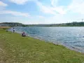 Ein sonniger Tag am Dortmunder See. Menschen spazieren am Ufer entlang, während ein Paar auf dem Gras sitzt und die Aussicht genießt.