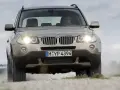 Złoty SUV BMW X3 z włączonymi światłami jedzie po szutrowej drodze, unosząc kurz. To jeden z najbardziej komfortowych aut na drodze.
