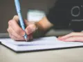 Dłoń pisze niebieskim długopisem w notatniku. Może tworzy nowy **akronim** do zapamiętania.
