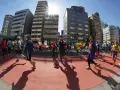 Atleti corrono nella maratona di Tokyo, circondati da grattacieli moderni sotto un sole splendente.