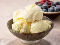 Pyszne, kremowe lody waniliowe w miseczce. Idealne na deser, gdy szukasz prostego przepisu na lody. W tle miska z jagodami i malinami.