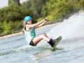 Dziewczyna w kasku i kamizelce pływa na wakeboardzie, tworząc wielki szelment wody.