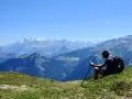 Un randonneur léger profite d'une vue panoramique sur les montagnes. Il est assis sur une colline verdoyante, bâton à la main, admirant le paysage majestueux.