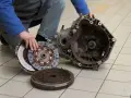 Mechanik prezentuje części po demontażu skrzyni biegów, przygotowując się do wymiany łożyska oporowego.