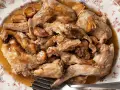 Conejo al ajillo servido en un plato con borde floral, con trozos de carne dorada y dientes de ajo enteros.