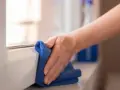 Mano pulisce davanzale in PVC effetto legno con panno blu. Scopri come pulire pvc effetto legno per mantenerlo come nuovo.
