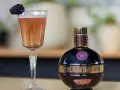 Chambord likier jak pić? Elegancki kieliszek z różowym drinkiem i jeżyną obok butelki likieru. Idealny na specjalne okazje.