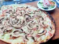 Tarta flambeada con champiñones y bacon, servida sobre tabla de madera. Una pequeña ensalada acompaña.