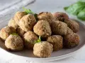 Un piatto pieno di polpette di melanzane dorate e croccanti, guarnite con prezzemolo fresco.