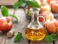 Aceto di mele in un decanter, mele rosse e foglie verdi su un tavolo di legno. Un rimedio naturale per sapere come eliminare i funghi della pelle velocemente.