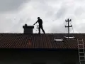 Kominiarz na dachu sprawdza komin. Zastanawiasz się, ile kosztuje przegląd kominiarski?