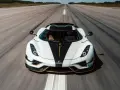 Biały Koenigsegg Regera z czarnym pasem i złotymi akcentami pędzi po pasie startowym, zostawiając za sobą smugę prędkości.