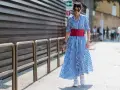 Donna con vestito a righe blu e bianche, cintura rossa e sneakers bianche cammina per strada.
