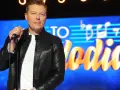 Rafał Brzozowski z mikrofonem na scenie, w tle napis "Jaka to melodia?".