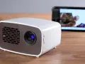 Kleiner Beamer mit Handy verbinden für Heimkino. Ein Smartphone zeigt ein Bild, während der Beamer bereit ist.