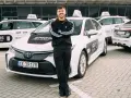Młody mężczyzna w dresie stoi przed białymi samochodami Uber z napisem "ERES Partner". To jego praca prywatny kierowca.