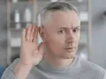 Mężczyzna z siwymi włosami przykłada dłoń do ucha, próbując usłyszeć. Czy to początek zawalu ucha?