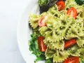 Ein köstlicher Nudelsalat mit Pesto, garniert mit frischen Kirschtomaten und Salatblättern.