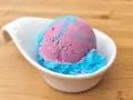 Ein Löffel eis mit kaugummi Geschmack, in rosa und blau, serviert in einer weißen Schale auf Holzuntergrund.