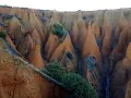 Paisaje erosionado con formaciones cónicas de tierra rojiza, vegetación escasa y un camino que parece el pontón de la oliva ruta circular.
