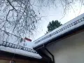 Dach stromy pokryty śniegiem, z drabinkami zabezpieczającymi przed lawinami. Gałęzie drzew wiszą nad nim.