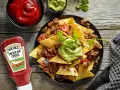 Nachos con carne, guacamole y salsa en un plato negro, con botella de Heinz y cuencos de salsa.