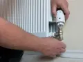 Wymiana zaworu w grzejniku bez spuszczania wody. Ręce majsterkowicza przykręcają nowy zawór termostatyczny.