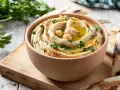 Hummus cremoso en cuenco de madera, decorado con garbanzos, aceite de oliva, perejil y pimentón.