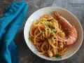 Spaghetti con gamberoni surgelati, un piatto gustoso e veloce. Un gamberone intero adorna la pasta condita con pomodorini e prezzemolo.