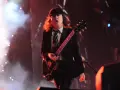 Ein Mann mit Hut und Schlagzeug spielt auf einer ACDC Gitarre, umgeben von Rauch und Lichtern.