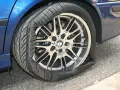 Un pneumatico squarciato sul cerchione di un'auto blu. La gomma è completamente sgonfia e deformata, mostrando il danno.