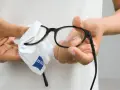 Här putsas glasögon med en mjuk trasa. En person håller i bågarna och putsar linserna med en vit trasa med Zeiss-logga.