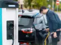 Mój elektryk czeka na ładowanie. Mężczyzna podłącza kabel do samochodu przy stacji ładowania.
