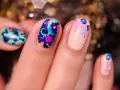 Comment avoir de beaux ongles : des ongles décorés de motifs floraux colorés et de petites étoiles sur fond bleu nuit ou nude.