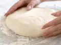 Mani che lavorano un impasto pizza veloce, soffice e pronto per essere steso.