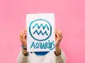 Waga i Wodnik: przyjaźń w kolorach tęczy. Ręce trzymają plakat z symbolem Wodnika i napisem "Aquarius" na różowym tle.