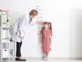Lekarka mierzy wzrost dziewczynki przy tablicy z podziałką.