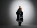 Uśmiechnięta kobieta w błyszczącej spódnicy i futrzanym płaszczu. Czy do filharmonii trzeba ubrać się elegancko? Ta stylizacja sugeruje, że tak!