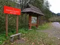 Czerwony znak "Rezerwat Przyrody Sine Wiry" i drewniana tablica informacyjna przy leśnej ścieżce.